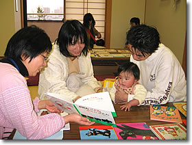 ブックスタートのようす。赤ちゃんを囲んで、お母さんが本を読み、ほかの大人が見守っていいます。